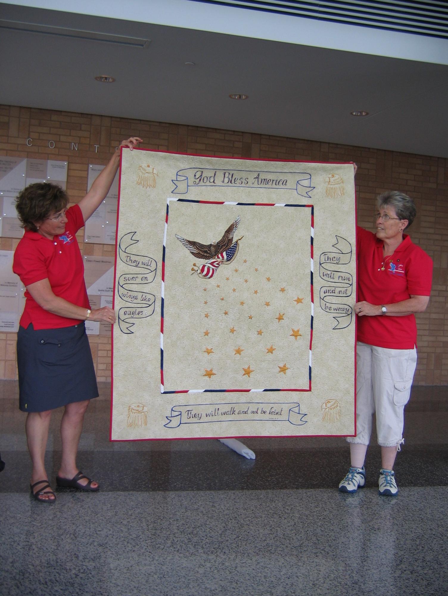 Two people holding a quilt for display. 