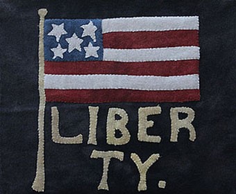 A flag with "Liberty" in block letters all appliqued on wool.