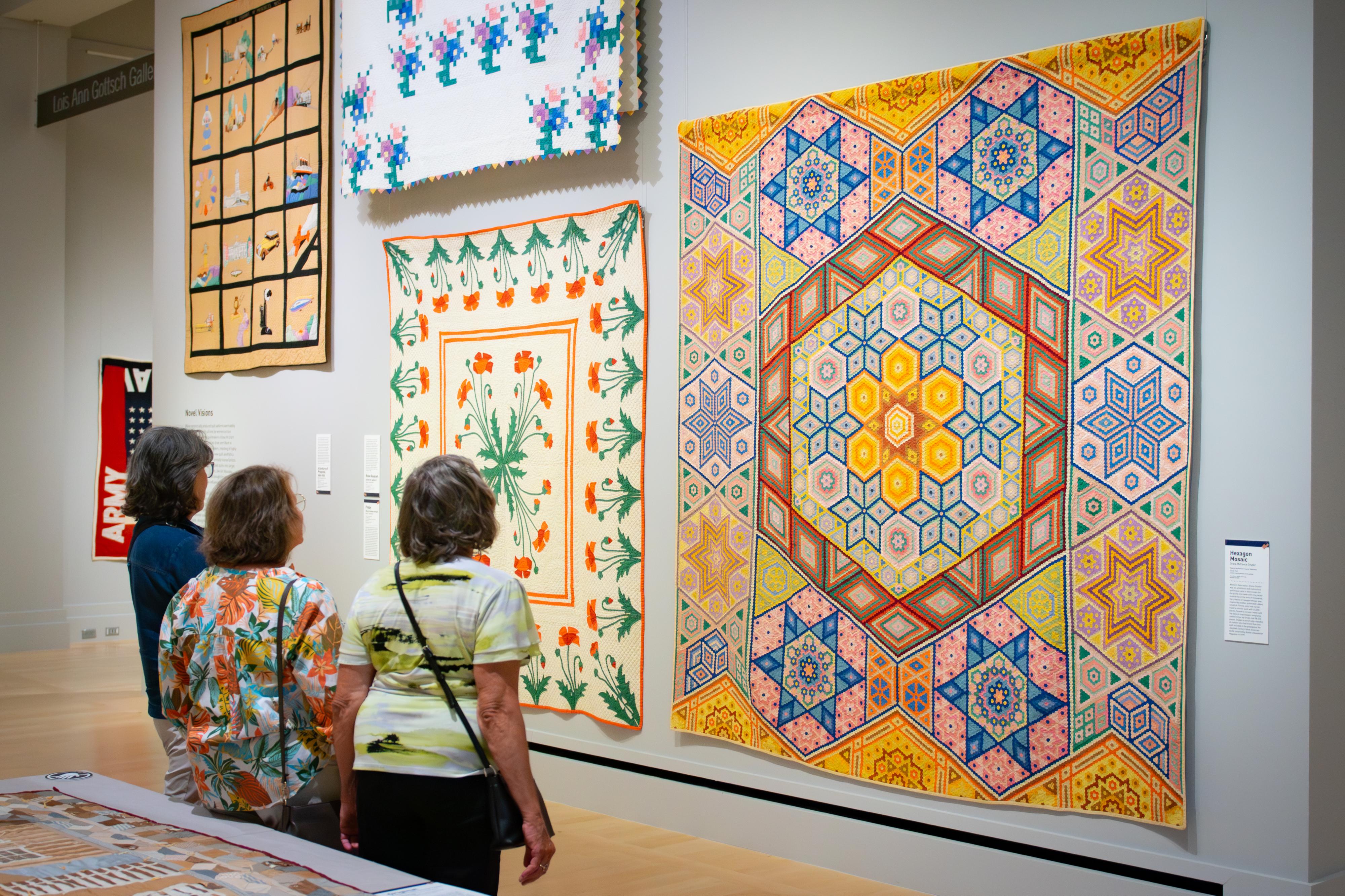 Three people looking at a quilt.